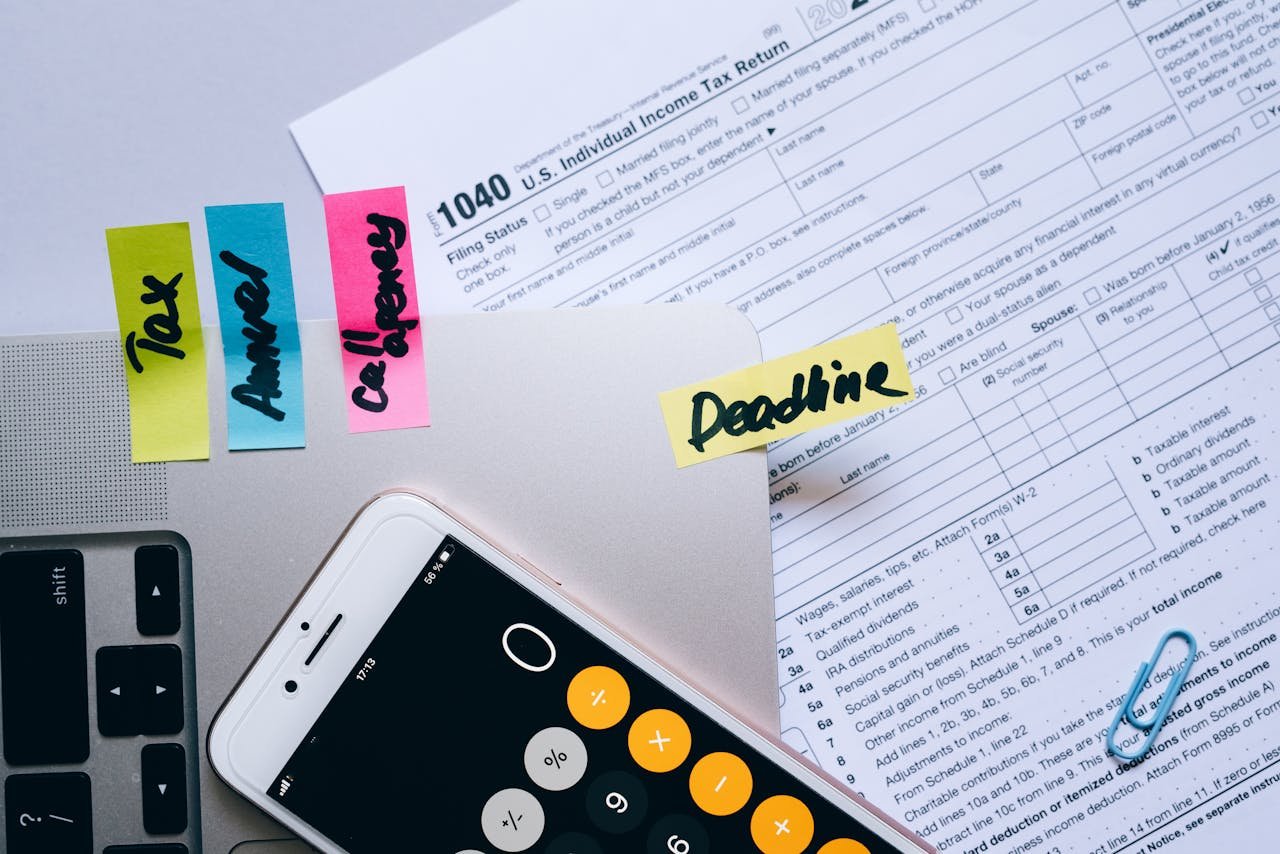 Offerings Office desk flat lay showing tax documents, calculator app on smartphone, sticky notes, and paperclips.